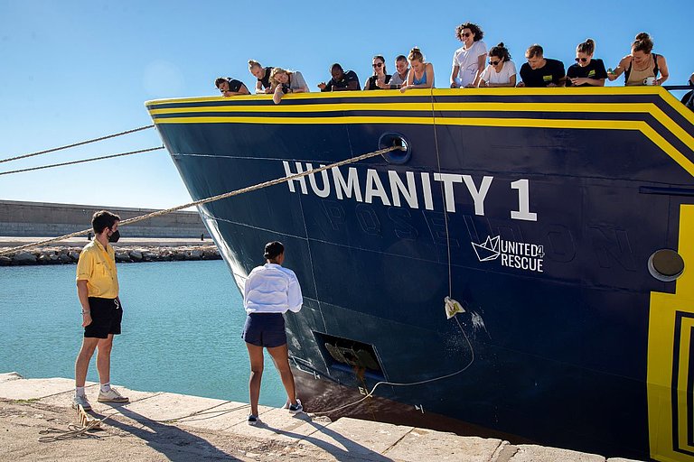 Mehrere Menschen stehen auf dem neuen Schiff von SOS Humanity während dieses getauft wird. 