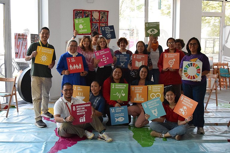 The picture shows a group of people looking into the camera and holding pictures of the 17 UN Sustainable Development Goals in their hands.