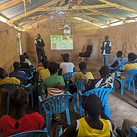 A group of people is sitting in chairs. They are watching a presentation.