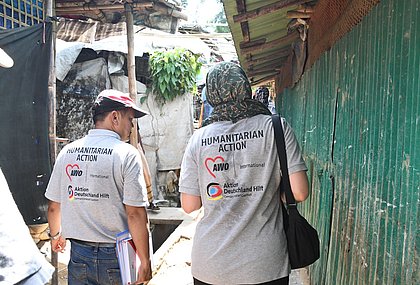 Zwei Menschen laufen, man sieht sie von Hinten. Sie tragen t-Shirts mit dem Logo von AWO International.