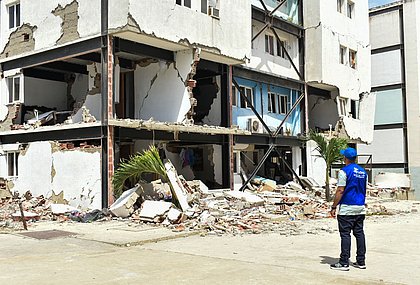 Ein Mitarbeiter von der Partnerorganisation FUDEP steht vor einem zerstörten Haus
