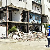 Ein Mitarbeiter von FUDEO steht vor einem zerstörten Haus