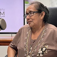 Eine ältere Frau spricht in ein großes Mikrofon einer Radiosendung.