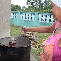 Eine Frau kocht Bohnen in einem großen Topf im Freien.