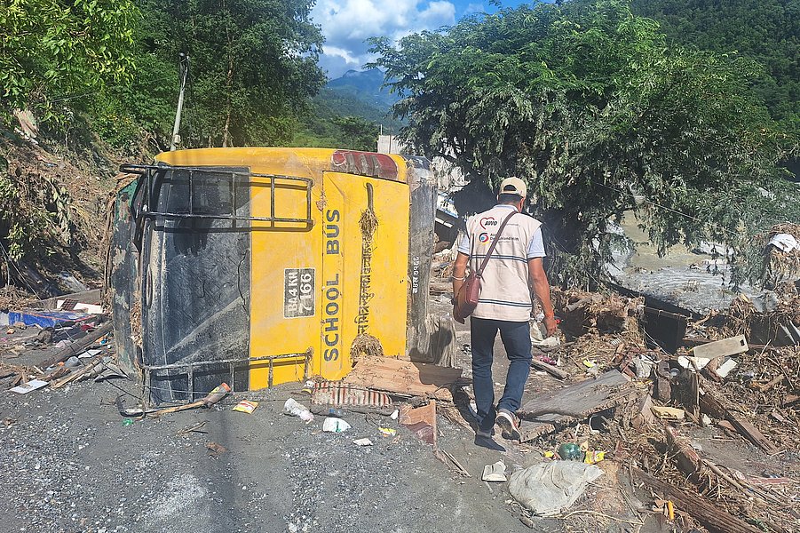 Mitarbeiter von AWO International vor Trümmern und einem umgestürzten Schulbus im Flutgebiet in Nepal