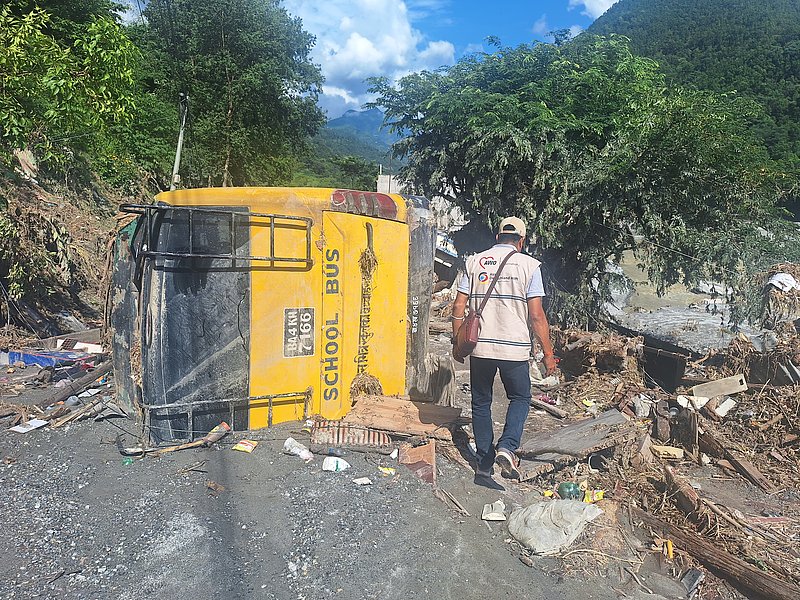 Mitarbeiter von AWO International vor Trümmern und einem umgestürzten Schulbus im Flutgebiet in Nepal