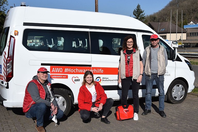 4 AWO employees and volunteers are standing in front of a white bus. The bus is marked "AWO Hochwasserhilfe" (AWO flood relief).