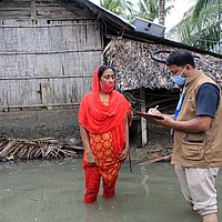 Mann und Frau stehen in einem überfluteten Durchgang, Mann notiert auf Klemmbrett