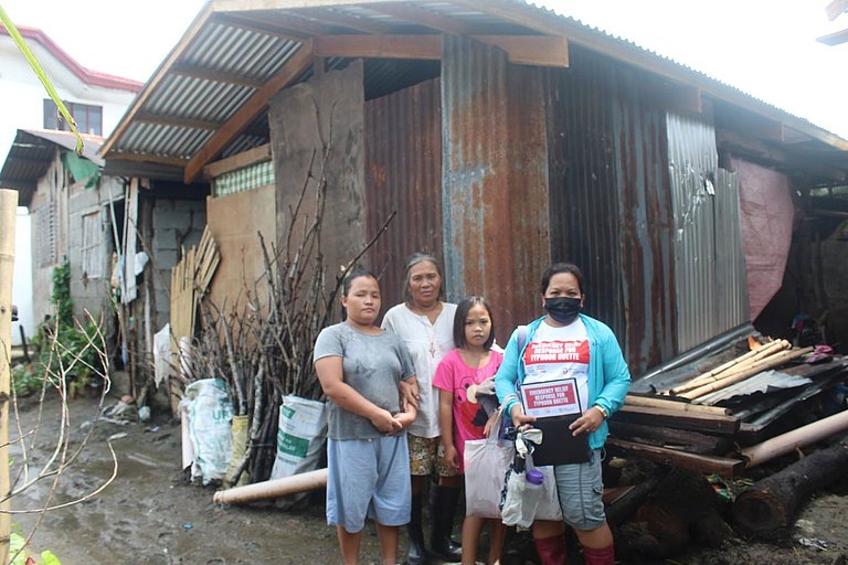 Two women and two girls are standing in front of a damages house.