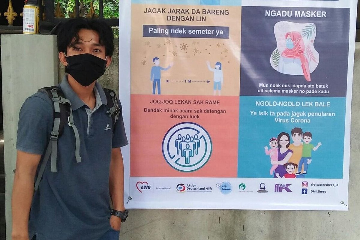 Boy with face masks standing next to banner concerning Covid 19-protective measures 