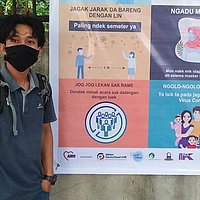 Junge mit Mundschutz steht neben einem Plakat