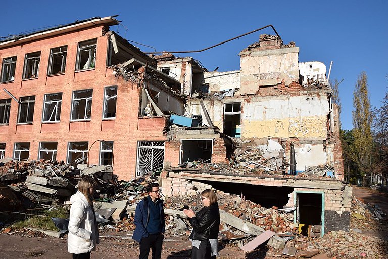 Drei Menschen stehen vor dem zerstörte Gebäude 