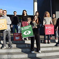 The picture shows a group of people holding paper pads with the UN Sustainable Development Goals.