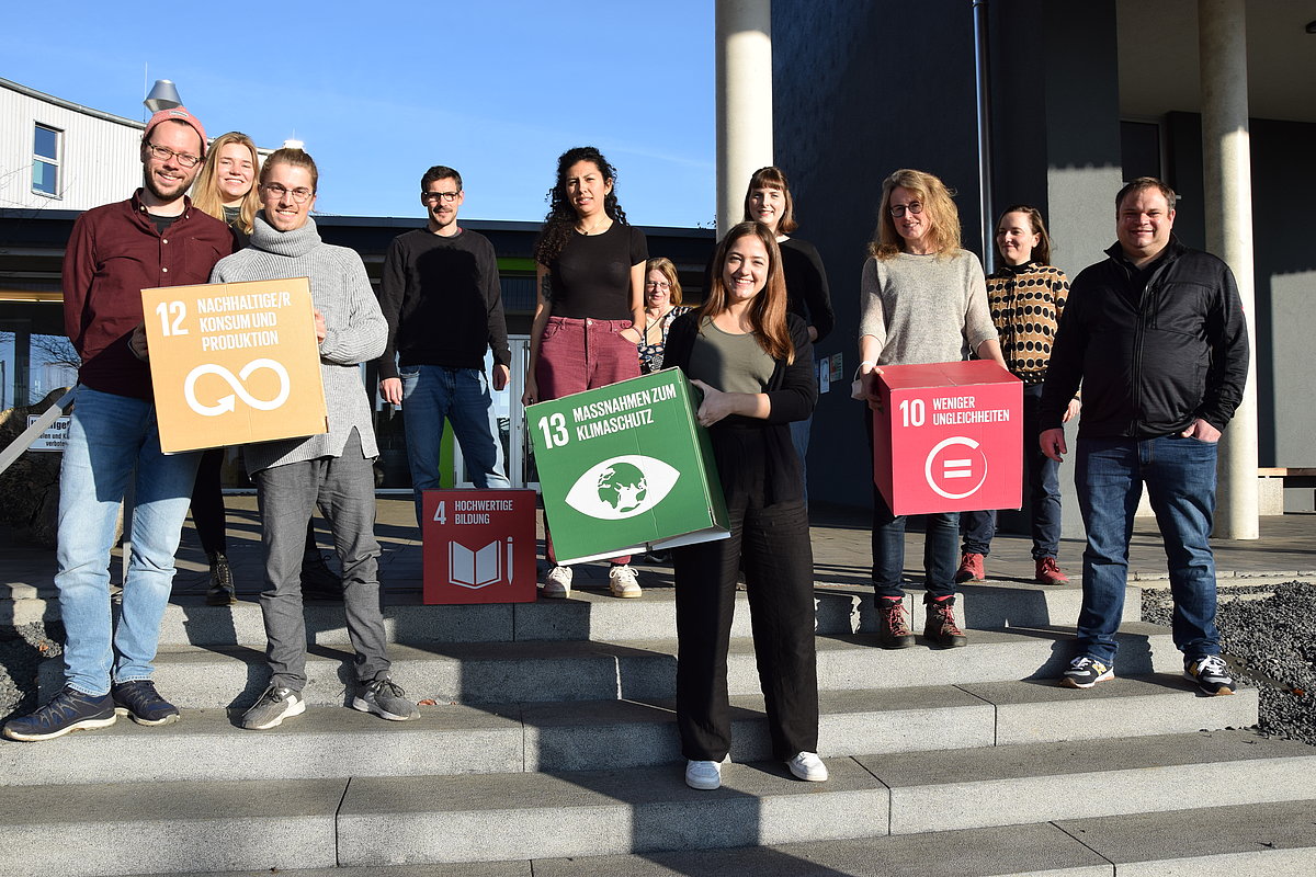 The picture shows a group of people holding paper pads with the UN Sustainable Development Goals.