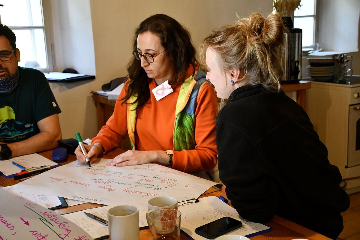 Two women. One is writing on a large sheet of paper.