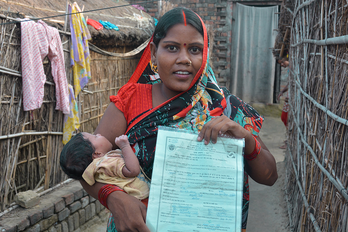 Frau mit Baby im Arm hält Dokument in die Kamera