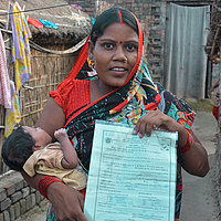 Woman with baby in her arms holds document in camera