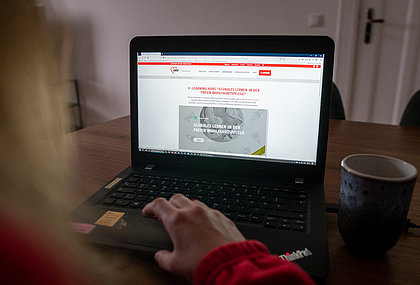 a woman sits in front of laptop where E-Online Course of AWO Int. is shown