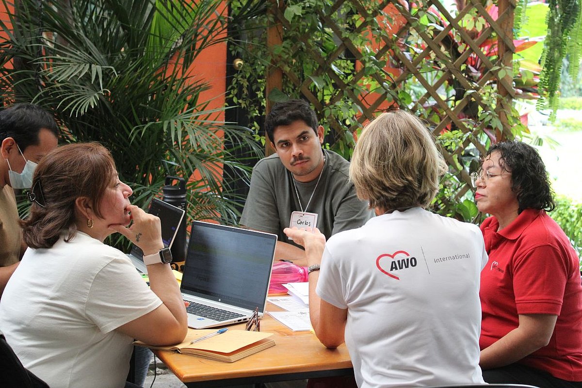 Vier Personen sitzen um einen Tisch mit Laptop und Arbeitsmaterialien herum und unterhalten sich.