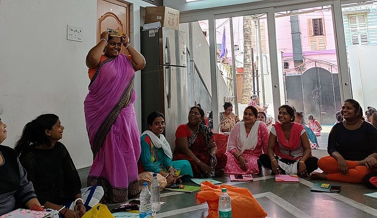 Frauen aus Indien sitzen auf dem Boden, eine Frau steht und erzählt etwas