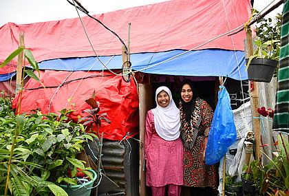 Two women are standing in front of a tent, which is their temporary shelter.