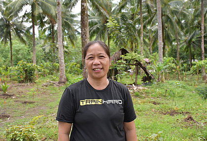 A woman stands in front of a field and smiles at the camera.