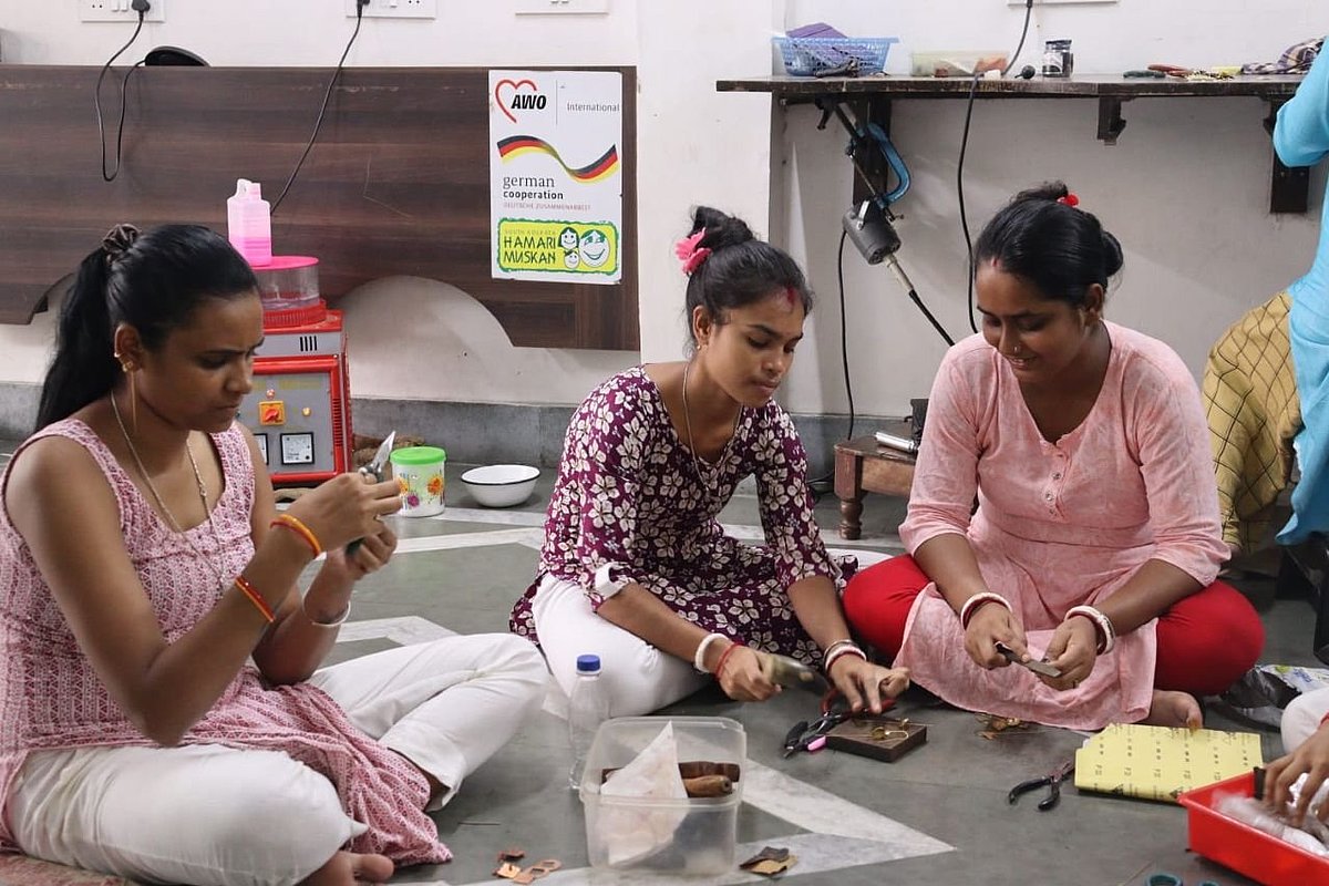 Three women are sitting on the floor doing some handicraft work.