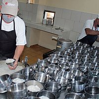 Zwei Mitarbeitende portionieren Mahlzeiten in Dosen. 