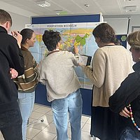 Auf dem Bild sind Menschen zu sehen, die vor einer Landkarte stehen.