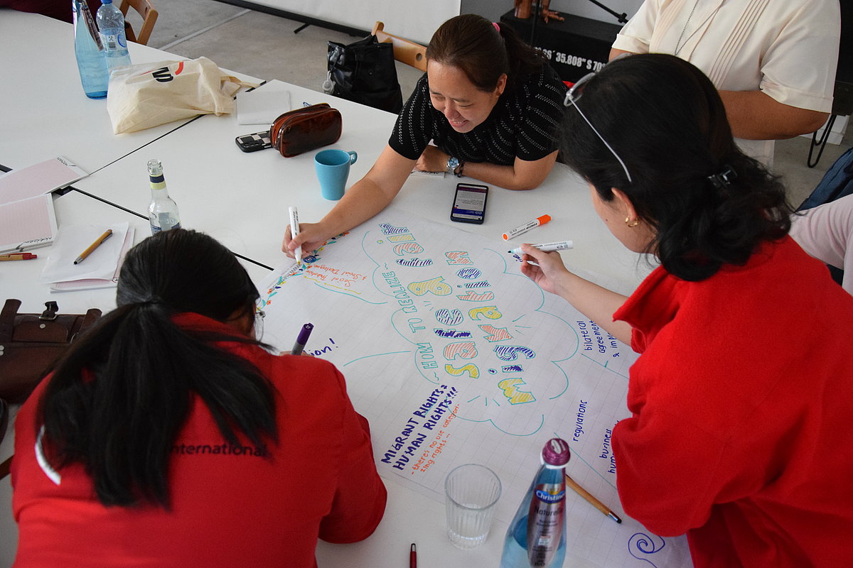 The picture shows three women writing something together on a poster.